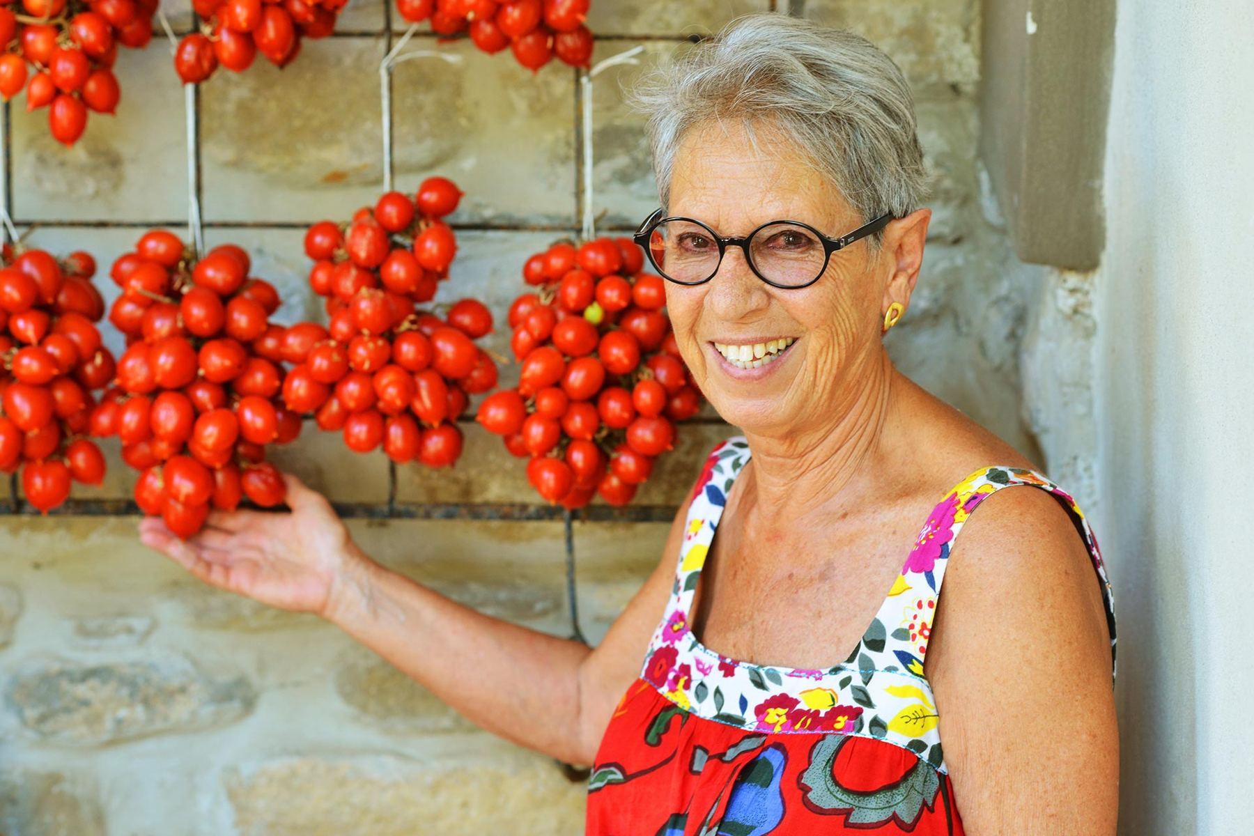 Eine Frau aus dem Cilento vor einer Wand mit aufgehängten Tomatenrispen.